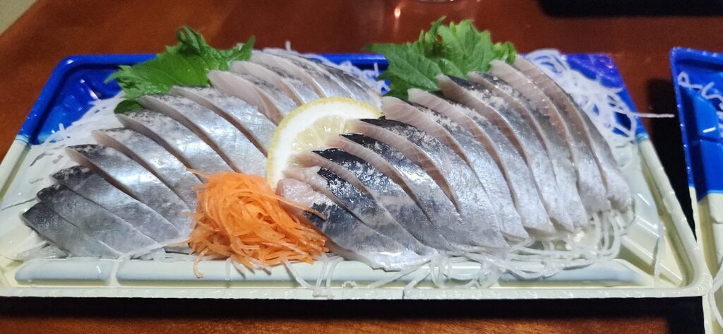 Tray of sliced silver skinned fish sashimi with lemon, shiso leaves and shredded radish