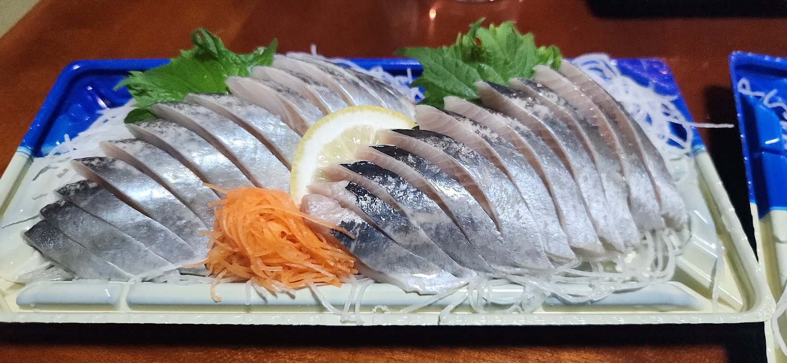 Tray of sliced silver skinned fish sashimi with lemon, shiso leaves and shredded radish