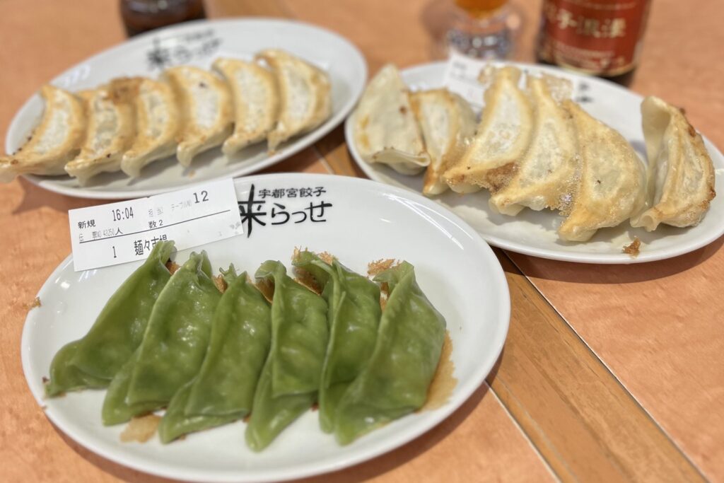 Three plates of Utsunomiya gyoza, including green dumplings, on a table at Kirasse